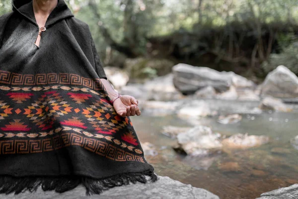 Hand of a young man meditating by the river sitting on a rock. Close up. Concept of spiritualism in the nature.