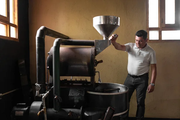 A Hispanic man is inspecting a small coffee roaster machine. Concept of local coffee production