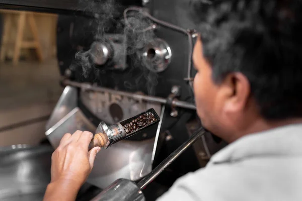 İspanyol bir adam kahve kızartma makinesindeki fasulyeleri kontrol ediyor. Yerel kahve üretimi kavramı