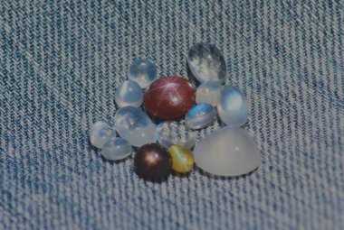 Closeup view of gemstones including star ruby, star sapphire, cats eye and blue moonstones kept on a denim cloth clipart