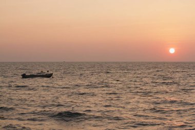view from seashore during a clear sunset with some boats in the horizon