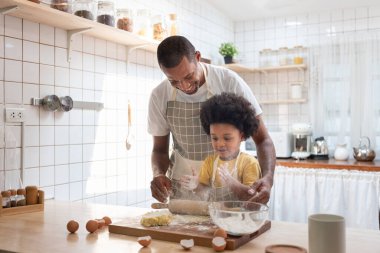 Afrikalı Amerikalı baba ve oğlu evde beyaz mutfakta fırın yaparken un oynamaktan zevk alıyorlar..