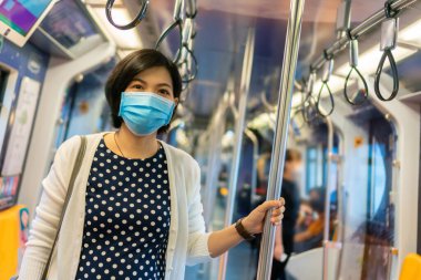 Korumalı yüz maskesi takan genç Asyalı kadın işe giderken trende ya da metroda duruyor..