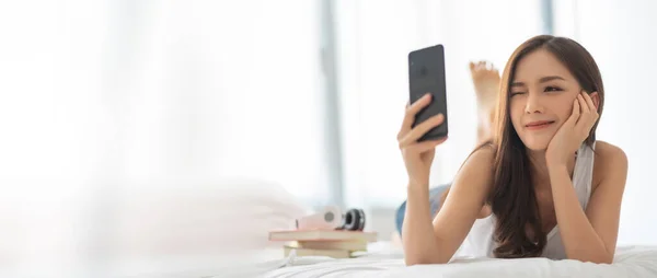 亚洲美女躺在床上 在手机或智能手机上自私自利 — 图库照片