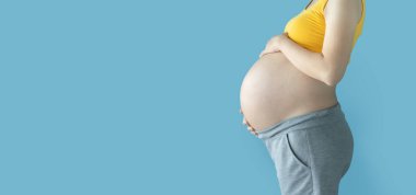 Mavi izole arka planda duran hamile kadın. Fotokopi çekilen hamileliği sırasında kadın karnına dokunuyor..