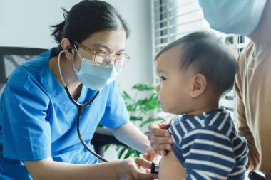 Tıp odasında steteskoplu küçük bir çocuğun akciğerlerini inceleyen Asyalı çocuk doktoru, doktor ya da hemşire..