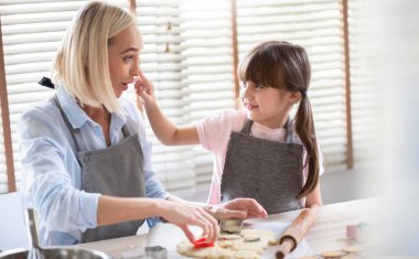 Neşeli gülümseyen kızım evde fırın yaparken annesiyle oynamaktan zevk alıyor. Eğlenceli bir aile mutfakta kek ya da kurabiye pişirirken eğleniyor..