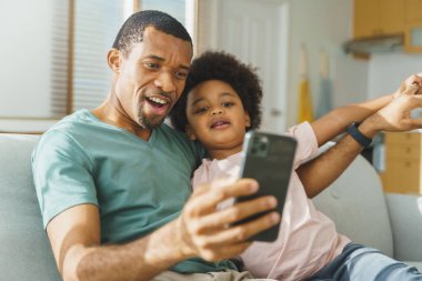 Happy Black African American father and his cute boy having video call on mobile phone at home