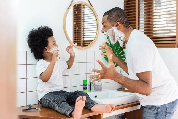 快乐的非洲裔美国父亲和小儿子一起在家里的浴室里嬉笑着在脸上刮泡沫 黑人家庭玩得很开心 — 图库照片