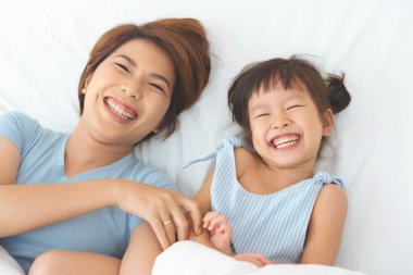 Mutlu Asyalı anne evde sevimli kızıyla eğleniyor ve gülüyor. Seçici bir şekilde kıza odaklanıyor.