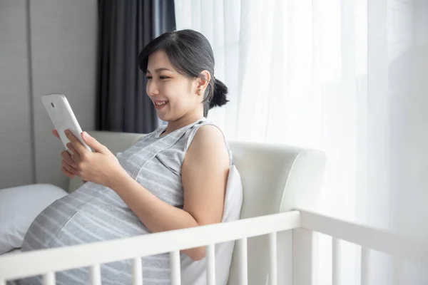 Ασιατική Νεαρή Έγκυος Γυναίκα Κρατώντας Ψηφιακό Δισκίο Κάθεται Στο Κρεβάτι — Φωτογραφία Αρχείου