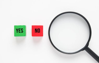 Yeşil tahta blokta evet, kırmızı tahta blokta hayır yazan bir büyüteç resmi. Karar verme kavramı