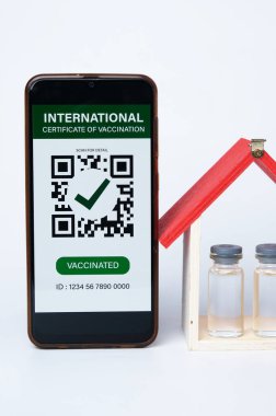 Üzerinde Uluslararası Aşı Sertifikası olan bir akıllı telefon resmi. Ayrıca Covid-19 aşısı ve ev minyatür içgörü.