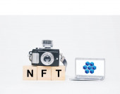 Miniaturní fotoaparát, notebook s blockchain, symbol éteria a slovo NFT. NFT je nezastupitelný žeton. Nezastupitelný žeton (NFT), který lze obchodovat a prodávat.