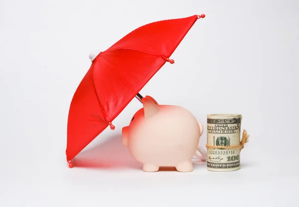 Tasarruf konseptini korumak için şemsiyeli ve sahte paralı bir kumbara resmi..