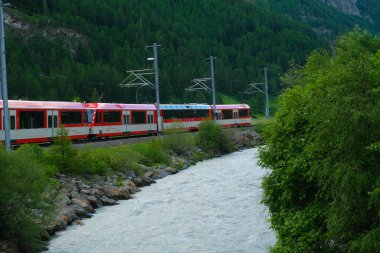 Selective focus picture with motion blur and noise effect part of red train at the railway with river insight.