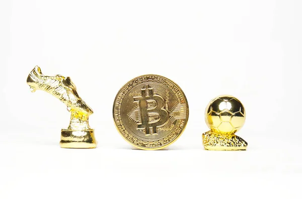 Selective focus picture of Bitcoin with miniature golden boot and golden ball on white background