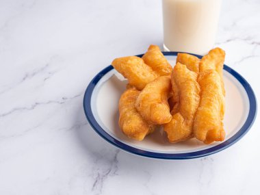 Yakın plan kızarmış hamur çubukları ya da beyaz tabakta Çin çöreği çubukları ve mermer masada bir bardak soya fasulyesi sütü. Metin için boşluk