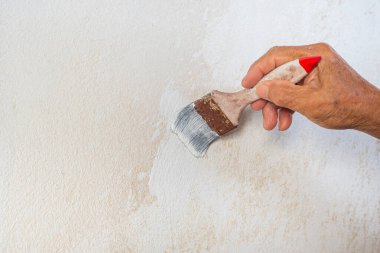 Banyodaki eski duvarda beyaz boyalı fırça tutan yaşlı adamın eli. Mesaj için yer var. Banyonun tadilatı.