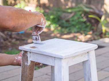 Son sınıf öğrencisi eski ahşap bir sandalyeyi fırçayla boyuyor. İnsan eli. Eski sandalyeler beyaza boyanır. Eski mobilyaların yenilenmesi