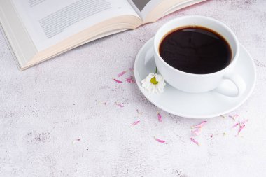 Bir fincan beyaz kahve, bir kitap ve gri taşlı arka planda çiçekler. Mesaj için yer var. Seçici odaklanma. Rahatlama zamanı. Rahatlama zamanı kavramı