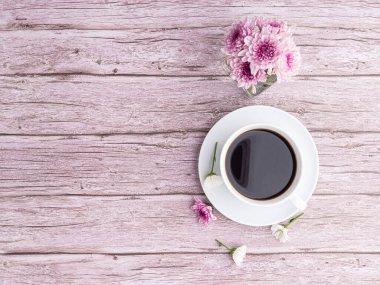 Bir fincan beyaz kahve ve ahşap masanın üzerindeki mor çiçeklerin üst görüntüsü. Mesaj için yer var. Seçici odaklanma. Rahatlama zamanı. Rahatlama zamanı kavramı