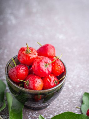 Seramik bir kasede, gri bir arka planda yaprakları olan olgun kırmızı kirazlar. Mesaj için yer var. Tatlı organik meyveler. Sağlıklı meyve kavramı.