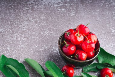 Seramik bir kasede, gri bir arka planda yaprakları olan olgun kırmızı kirazlar. Mesaj için yer var. Tatlı organik meyveler. Sağlıklı meyve kavramı.