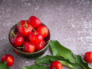 Tahta bir masada yapraklarla seramik bir tabakta olgun kırmızı kirazlar. Mesaj için yer var. Tatlı organik meyveler. Sağlıklı meyve kavramı.