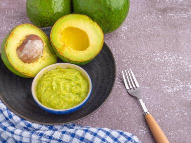 Tohumlu organik avokado, avokado yarımları, ve siyah tabakta taze guacamole mermer zemin üzerinde kumaş ve çatal bıçak. Üst Manzara. Mesaj için yer var. Düz yatış stili. Sağlıklı meyve kavramı..