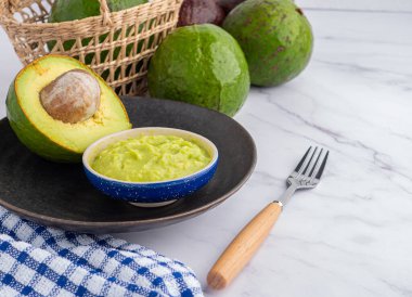 Tohumlu organik avokado, avokado yarımları, ve siyah tabakta taze guacamole mermer zemin üzerinde kumaş ve çatal bıçak. Üst Manzara. Mesaj için yer var. Düz yatış stili. Sağlıklı meyve kavramı..