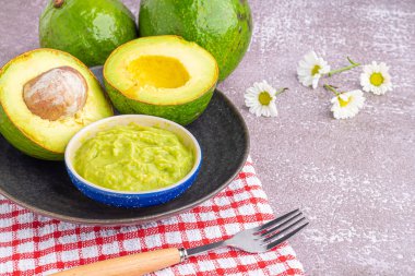 Tohumlu organik avokado, avokado yarımları, ve siyah tabakta taze guacamole mermer zemin üzerinde kumaş ve çatal bıçak. Üst Manzara. Mesaj için yer var. Düz yatış stili. Sağlıklı meyve kavramı..