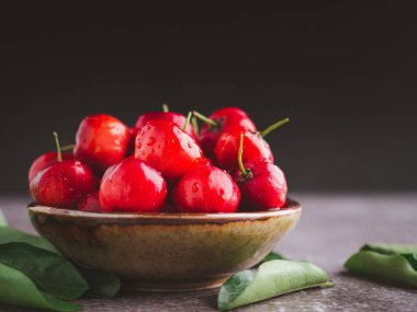 Tahta bir masada yapraklarla seramik bir tabakta olgun kırmızı kirazlar. Mesaj için yer var. Tatlı organik meyveler. Sağlıklı meyve kavramı.