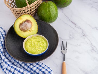 Tohumlu organik avokado, avokado yarımları ve siyah bir tabakta misket masasında kumaş ve çatal bıçakla taze guacamole. Üst Manzara. Mesaj için yer var. Düz yatış stili. Sağlıklı meyve kavramı..