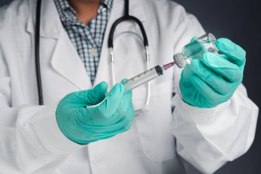 Elinde şırınga ve COVID-19 aşı şişesi olan bir doktor. Bağışıklık aşısı ve koronavirüs enfeksiyonunun tedavisi. Ön manzara. Tıbbi konsept ve koronavirüsle mücadele.