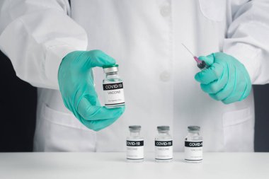 Laboratuvarda bir doktor ya da bilim adamı aşı geliştirmek ve araştırmak için şırıngayı aşı şişesiyle tutuyor. Tıbbi konsept ve virüse karşı savaş.