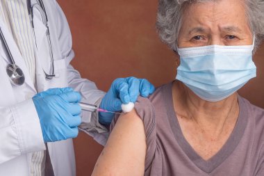 Doktor, kovid 19 salgını sırasında yüz koruyucu maske takarken yaşlı bir kadına iğne yapıyor. Son sınıf aşısı ve sağlık hizmeti kavramı.