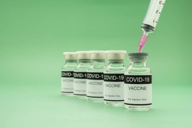 Cam şişelerdeki COVID-19 aşısı yeşil arka planda bir şırıngayla yerleştirilmiş. Bağışıklık aşısı ve koronavirüs enfeksiyonunun tedavisi. Tıbbi ve sağlık hizmetleri kavramı.