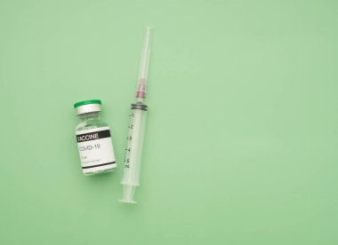Yeşil arka plana yerleştirilmiş cam şişe ve şırıngayla Covid-19 aşısı yakın plan. Koronavirüs enfeksiyonundan korunma, aşılama ve tedavi aşısı. Tıbbi konsept.