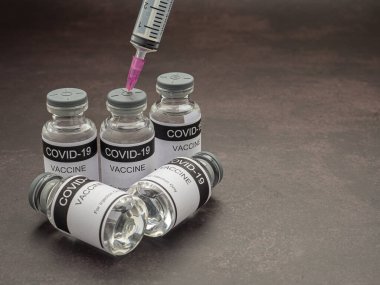 Cam şişelerde COVID-19 aşısı. Koyu taştan bir arka plana şırınga yerleştirilmiş. Bağışıklık aşısı ve koronavirüs enfeksiyonunun tedavisi. Üst Manzara. Tıbbi ve sağlık hizmetleri kavramı.