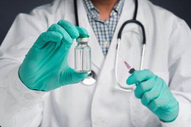 Elinde şırınga ve aşı şişesi tutan bir doktor. Bağışıklık aşısı ve virüs enfeksiyonuna karşı tedavi. Ön manzara. Tıbbi konsept ve virüse karşı savaş