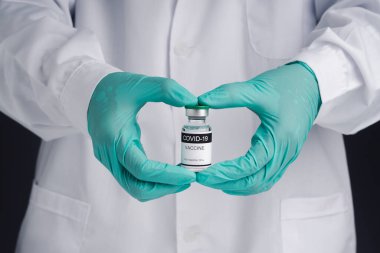 Doktor cam bir şişede COVID-19 aşısı gösteriyor. Bağışıklık aşısı ve koronavirüs enfeksiyonunun tedavisi. Ön manzara. Tıbbi konsept ve koronavirüsle mücadele.