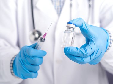 Elinde aşı şişesi ve şırıngası olan bir doktor gri arka planda duruyor. Bağışıklık aşısı ve virüs enfeksiyonuna karşı tedavi. Tıbbi konsept ve virüse karşı savaş.