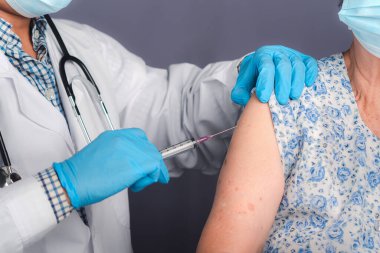 Yaşlı bir kadına iğne yapan doktor yüz maskesi takıyor. Yaşlı bir hasta, risk grubunda olduğu için hastanede COVID-19 aşısı yaptırıyor..