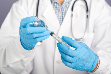Beyaz üniformalı bir doktor, şırınga tutan tıbbi eldivenler ve aşı için hazırlanan aşı şişesi. Bağışıklık aşısı ve koronavirüs enfeksiyonu tedavisi.