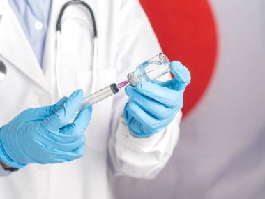 Bir doktorun elinde aşı şişesi ve şırıngayla Japon bayrağının arka planına karşı aşı hazırlıyor. Virüs enfeksiyonuna karşı aşı ve tedavi.
