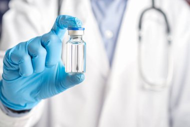 Doktor gri arka planda dururken aşı şişesini gösteren bir üniforma giyiyor. Bağışıklık aşısı ve virüs enfeksiyonuna karşı tedavi. Tıbbi konsept ve virüse karşı savaş.