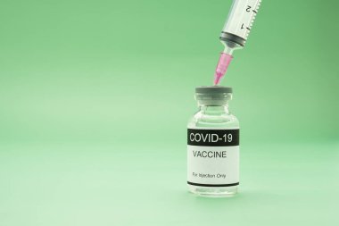 Cam şişedeki COVID-19 aşısı yeşil arka planda bir şırıngayla yerleştirilmiş. Bağışıklık aşısı ve koronavirüs enfeksiyonunun tedavisi. Tıbbi ve sağlık hizmetleri kavramı.