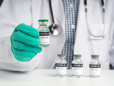 Elinde COVID-19 aşı şişesi tutan bir doktor. Bağışıklık aşısı ve koronavirüs enfeksiyonunun tedavisi. Ön manzara. Tıbbi konsept ve koronavirüsle mücadele