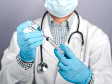 Beyaz üniformalı bir doktor, şırınga tutan tıbbi eldivenler ve aşı hazırlamak için COVID-19 aşı şişesi. Bağışıklık aşısı ve koronavirüs enfeksiyonu tedavisi.